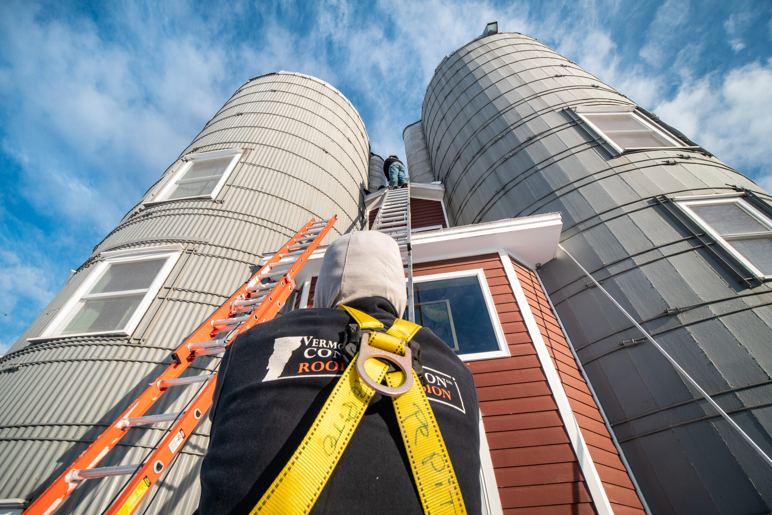 Vermont Construction Company roofer climbing up a ladder between two barn silos to perform a roof inspection
