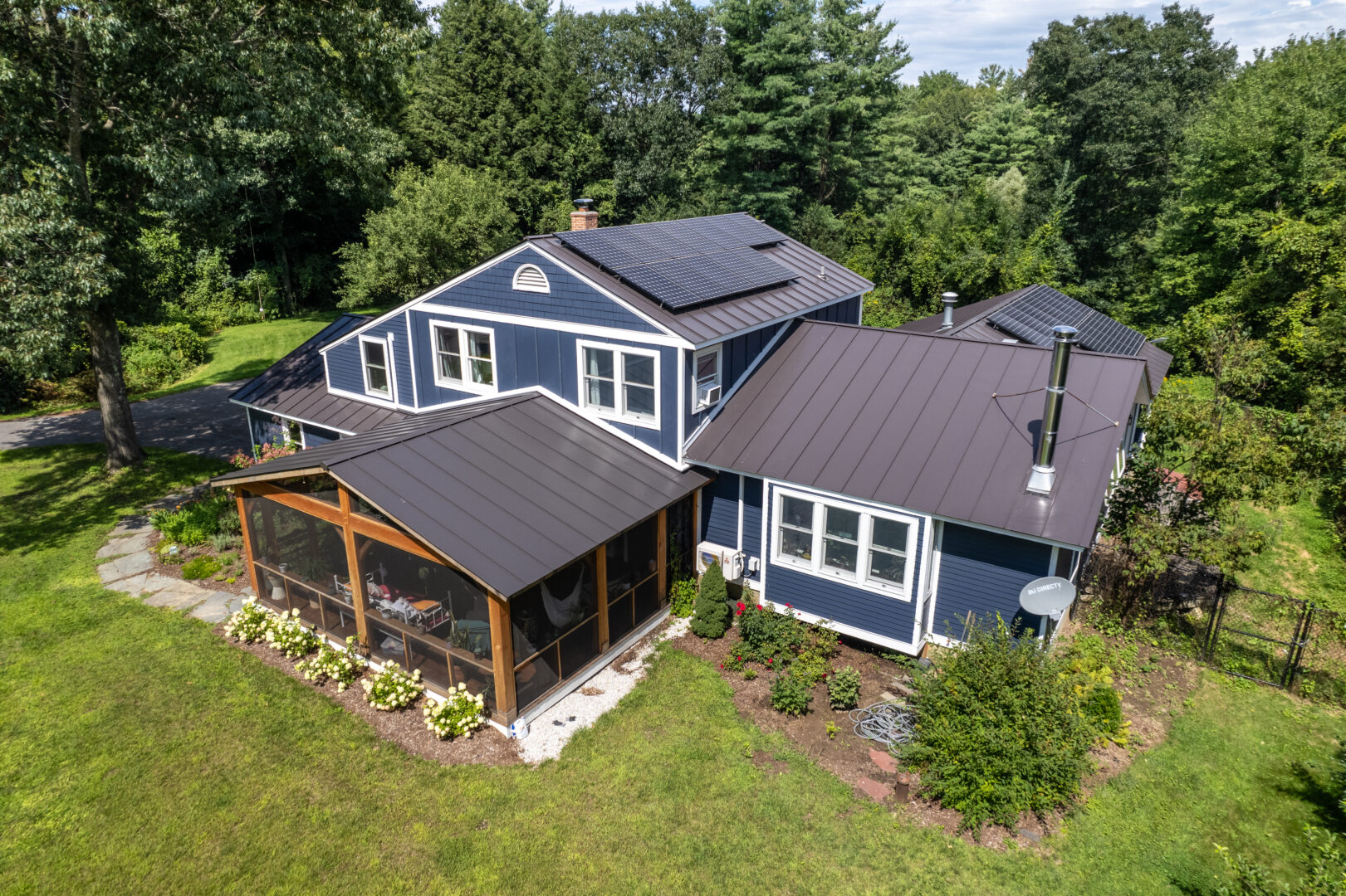 Aerial view of a blue house in Vermont with a stunning standing seam metal roof and solar panels