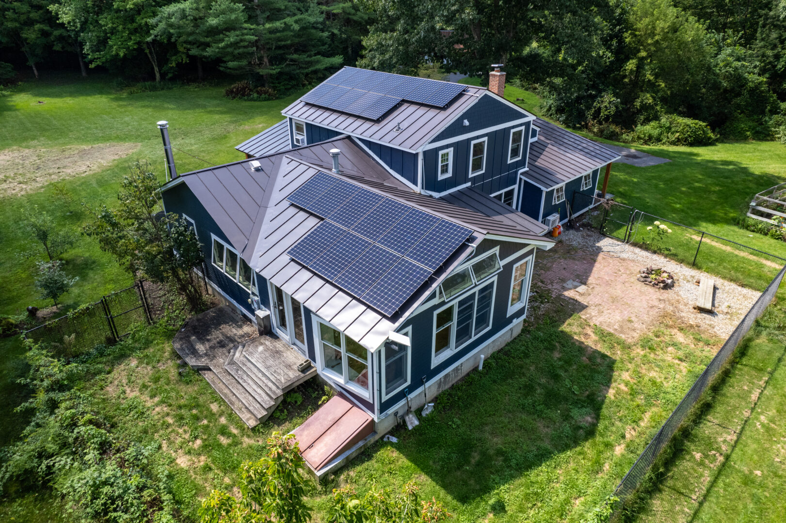 Aerial view of a blue house in Vermont with a standing seam metal roof and solar panels